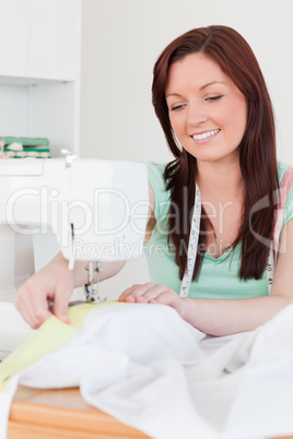 Cute red-haired female using a sewing machine in the living room