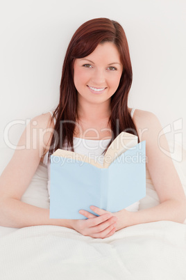 Good looking red-haired female reading a book while sitting on h