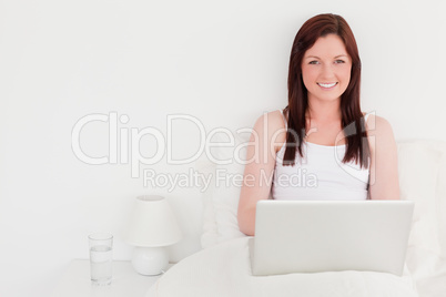 Attractive red-haired woman relaxing with her laptop while sitti