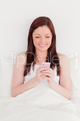 Beautiful red-haired woman writing a text on her mobile while si