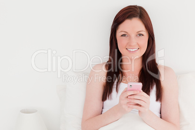 Pretty red-haired woman writing a text on her mobile while sitti