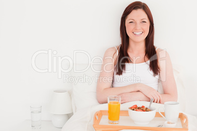 Beautiful red-haired woman having her breakfast while sitting on