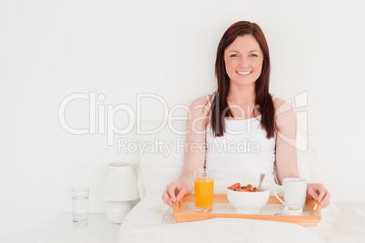 Attractive red-haired woman having her breakfast while sitting o