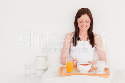 Pretty red-haired woman having her breakfast while sitting on he