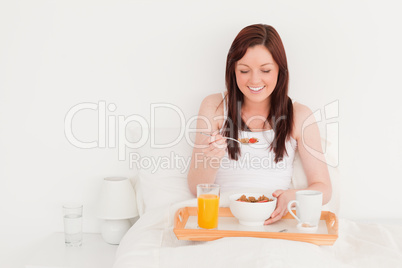 Beautiful red-haired female having her breakfast while sitting o