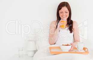Beautiful red-haired female drinking a glass of orange juice whi