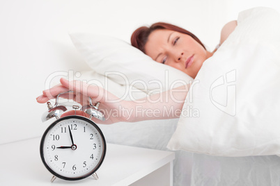 Attractive red-haired female waking up thanks to an alarm clock