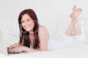 Beautiful red-haired female relaxing with her laptop while lying