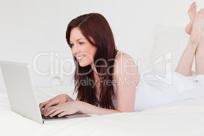 Attractive red-haired female relaxing with her laptop while lyin