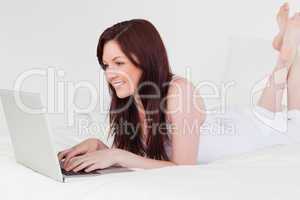 Attractive red-haired female relaxing with her laptop while lyin