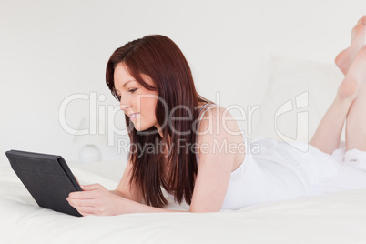 Attractive red-haired female relaxing with her tablet while lyin