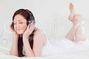 Pretty red-haired female relaxing with her headphones while lyin
