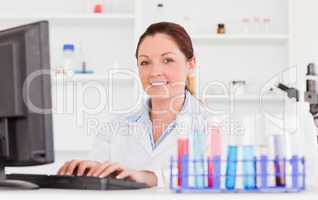 Red-haired scientist typing a report with her computer looking a