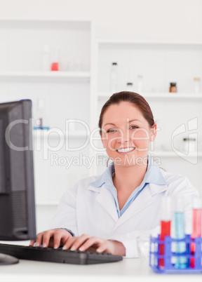 Smiling scientist typing a report with her computer looking at t