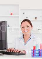 Smiling scientist typing a report with her computer looking at t