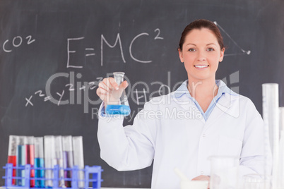 Cute scientist holding a container filled up with a blue liquid