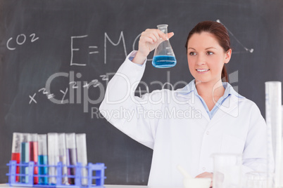 Cute scientist looking at a container filled up with a blue liqu