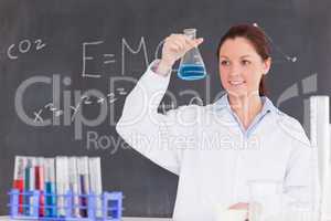 Cute scientist looking at a container filled up with a blue liqu