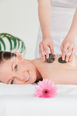 Smiling woman receiving a hot stone massage and a pink gerbera
