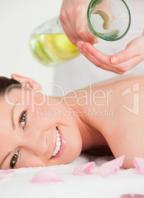Portrait of a young woman getting massage oil on her back in a s