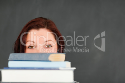 Close up of a young woman hidding behind a stack of books