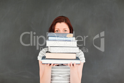 Cute youngh woman hidding herself behind a stack of books