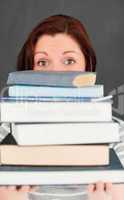 Young woman hidding behind a stack of books
