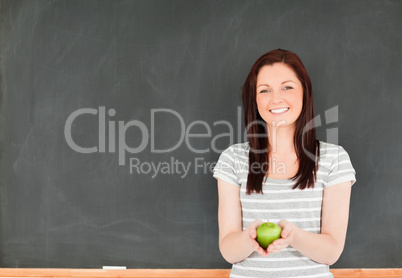 Beautiful young woman holding an apple against a blackboard