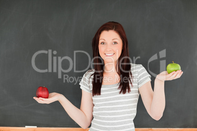 Cute woman with an apple on each hand against a blackboard