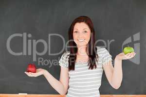 Cute woman with an apple on each hand against a blackboard