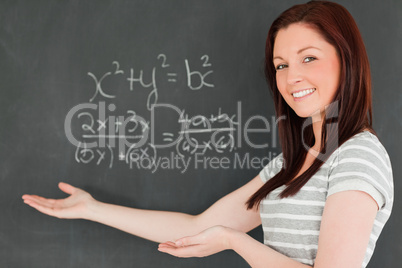 Beautiful young woman showing an equation on a blackboard