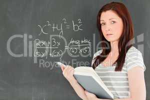 Cute woman trying to solve a mathematical equation on a blackboa