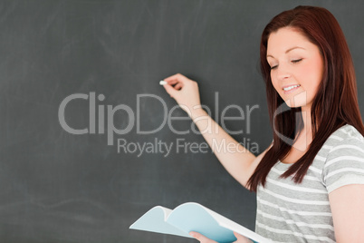 Focused young woman writting on a blackboard while looking at he