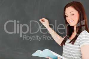 Focused young woman writting on a blackboard while looking at he