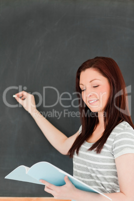 Cute woman writting on a blackboard while looking at her notes