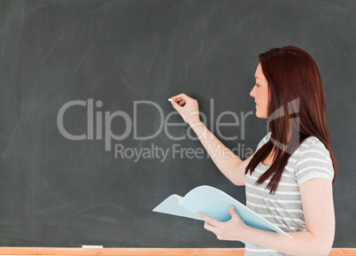 Young woman writting on a blackboard holding her notes