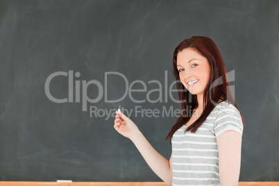 Smiling young woman standing in front of a blackboard with a pie