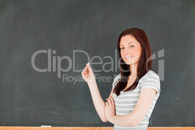 Young woman holding a piece of chalk while standing in front of