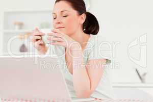 Good looking woman relaxing on her laptop while drinking a cup o