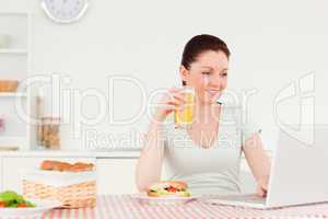 Smiling woman relaxing on her laptop and posing while drinking a