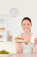 Portrait of a laughing young woman holding a sandwich and a glas