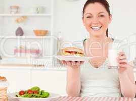Laughing young woman holding a sandwich and a glass of milk