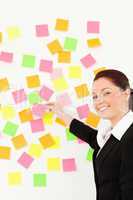 Smiling woman putting repositionable notes on a white wall