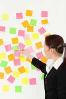 Woman putting colourful repositionable notes on a white wall