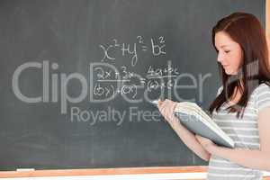 Gorgeous student looking at her notes while solving an equation