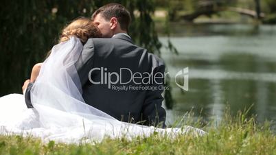 just married couple sitting embraced near pond