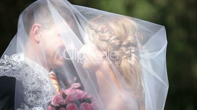 groom kissing bride under veil on  park alley