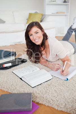 Young good looking woman writing on a notebook while lying on a