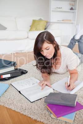 Young pretty woman writing on a notebook while lying on a carpet