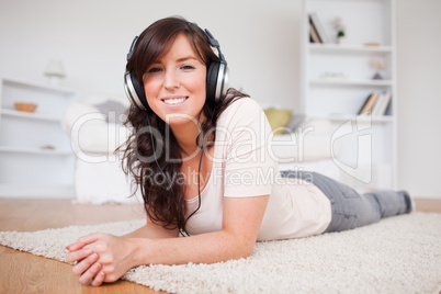 Charming brunette female using headphones while lying on a carpe